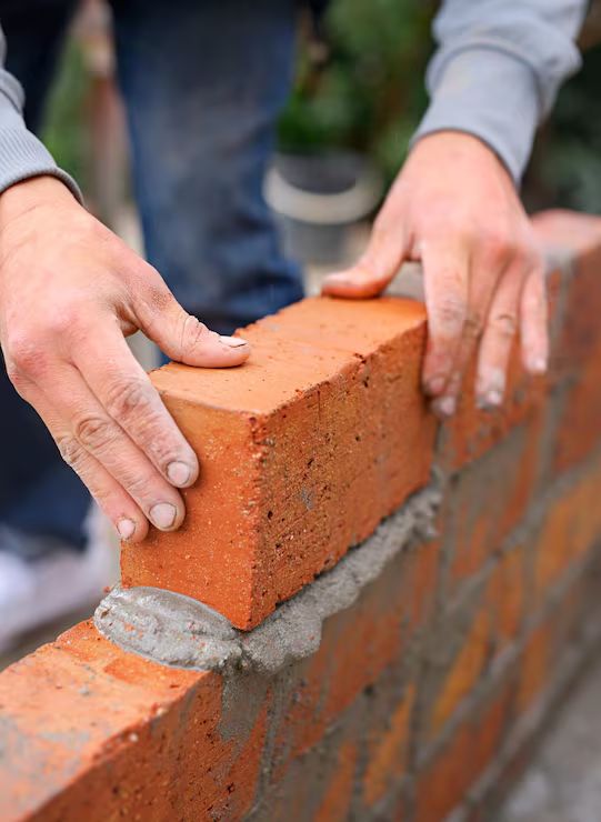 Hands bedding a brick onto a fresh mortar course